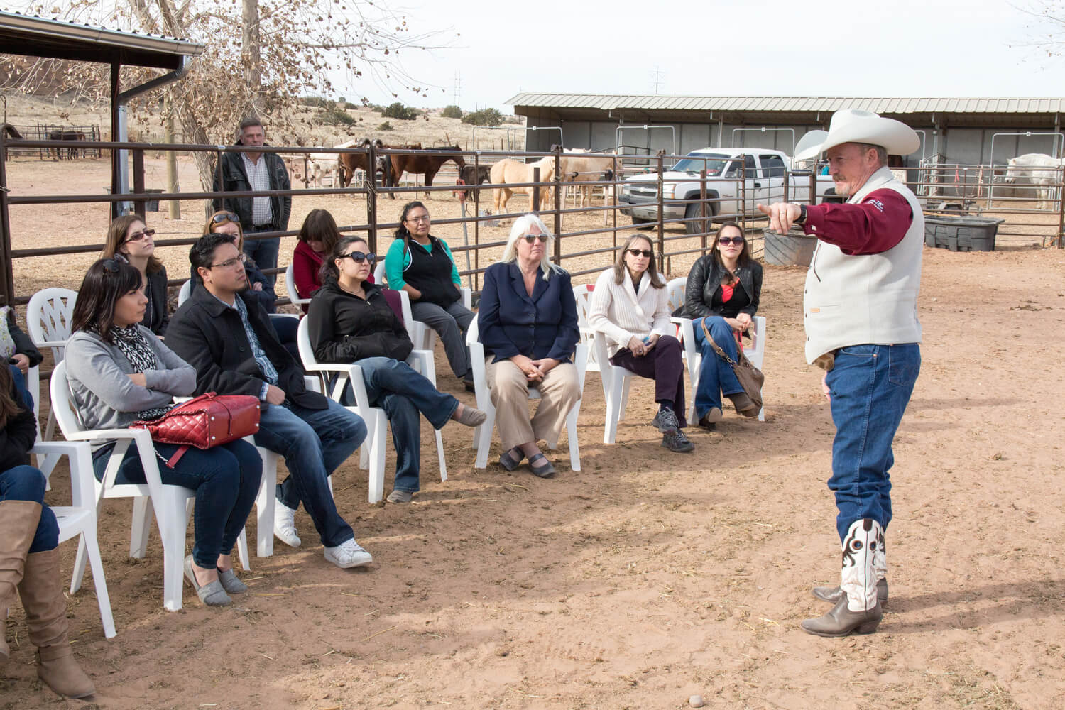 A man wearing a cowboy hat speaks to a small group of people outdoors