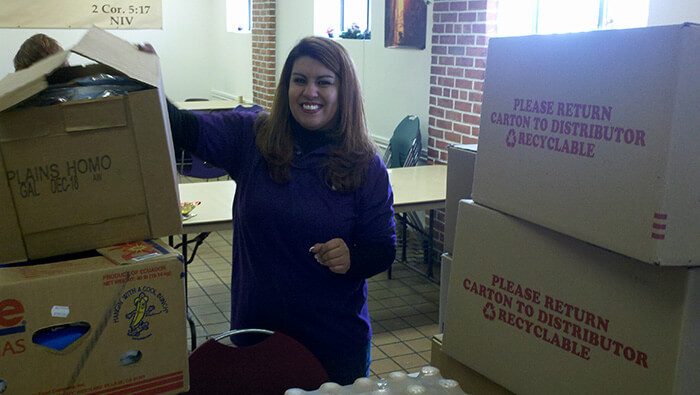 A woman smiles as she stands next to a box of supplies for Albuquerque Rescue Mission
